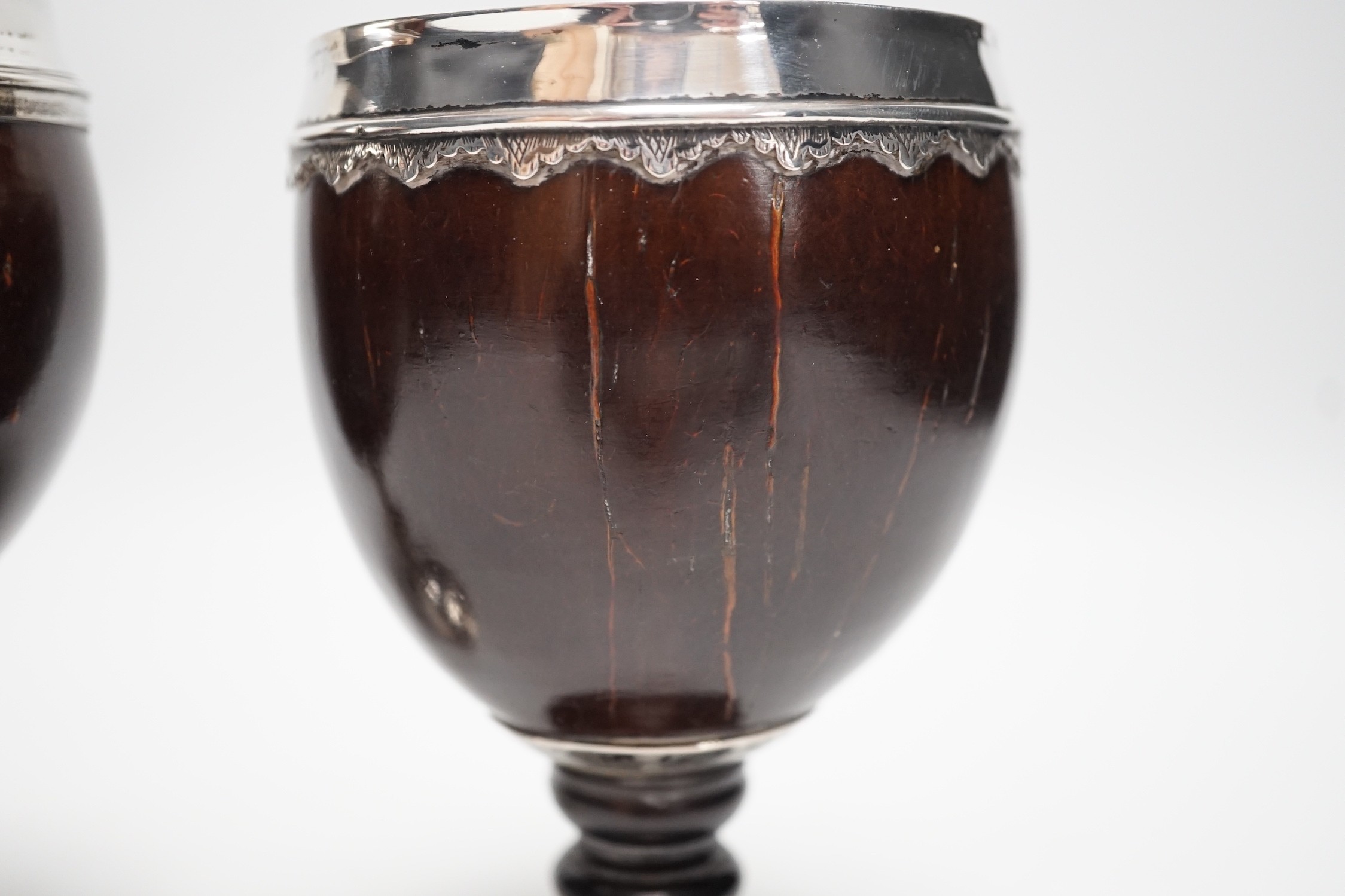 Two late 18th century white metal mounted pedestal coconut cups, one hallmarked silver for John Robbins?, London, 1764, 14.4cm, the other with white metal mounted top rim, on turned wooden base.